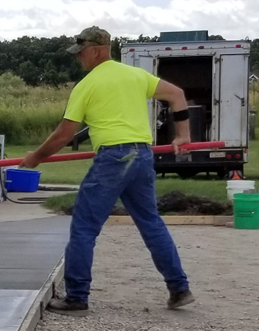 A man putting finish brushing on a fresh concrete driveway