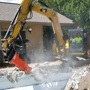 Excavator with breaker demolishing an old swimming pool